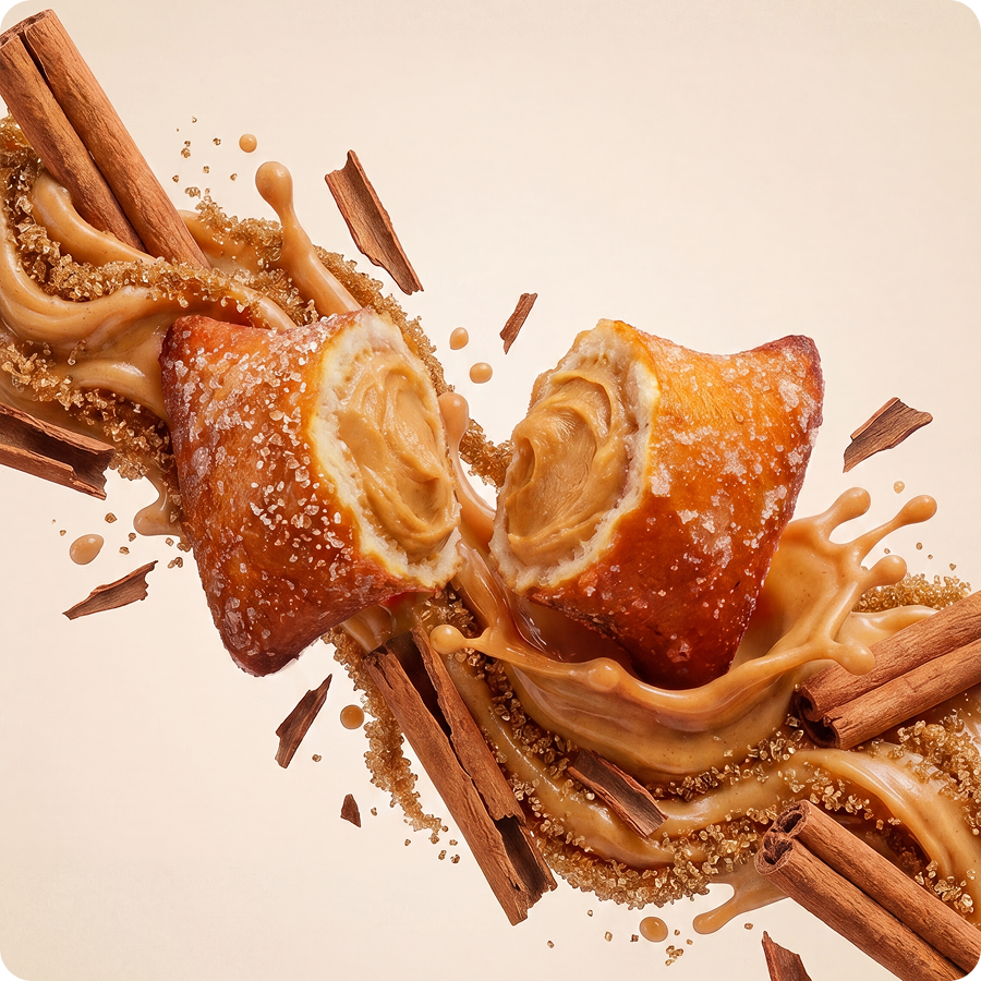 A cream-filled pastry split in half amidst a splash of caramel, cinnamon sticks, and brown sugar.