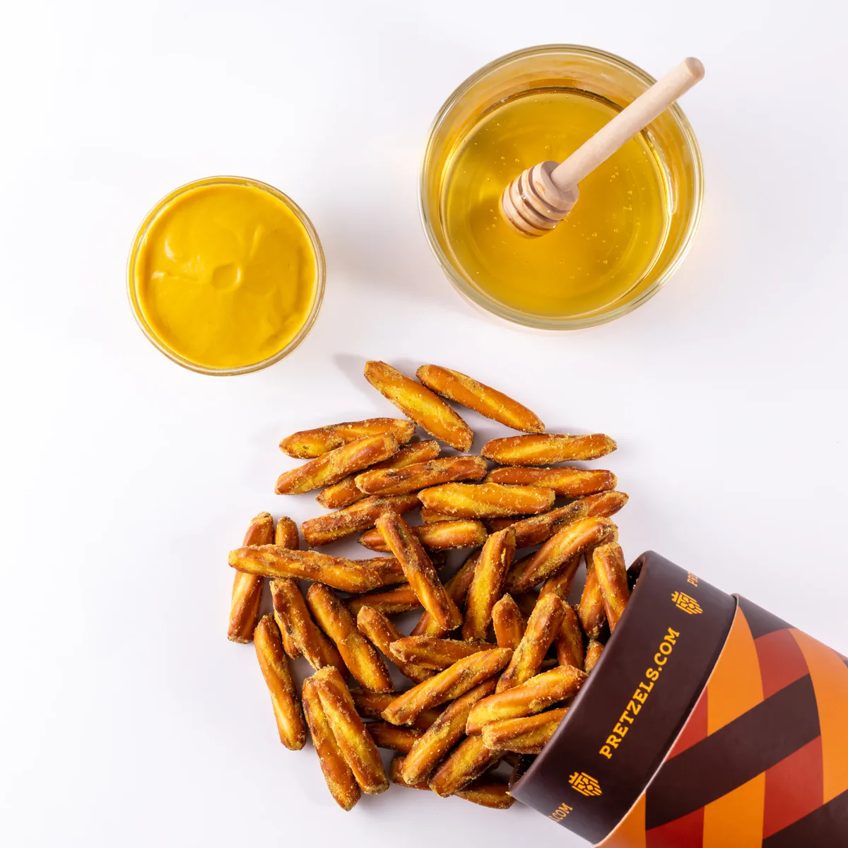 Pretzel sticks spilled from a container with bowls of mustard and honey nearby.