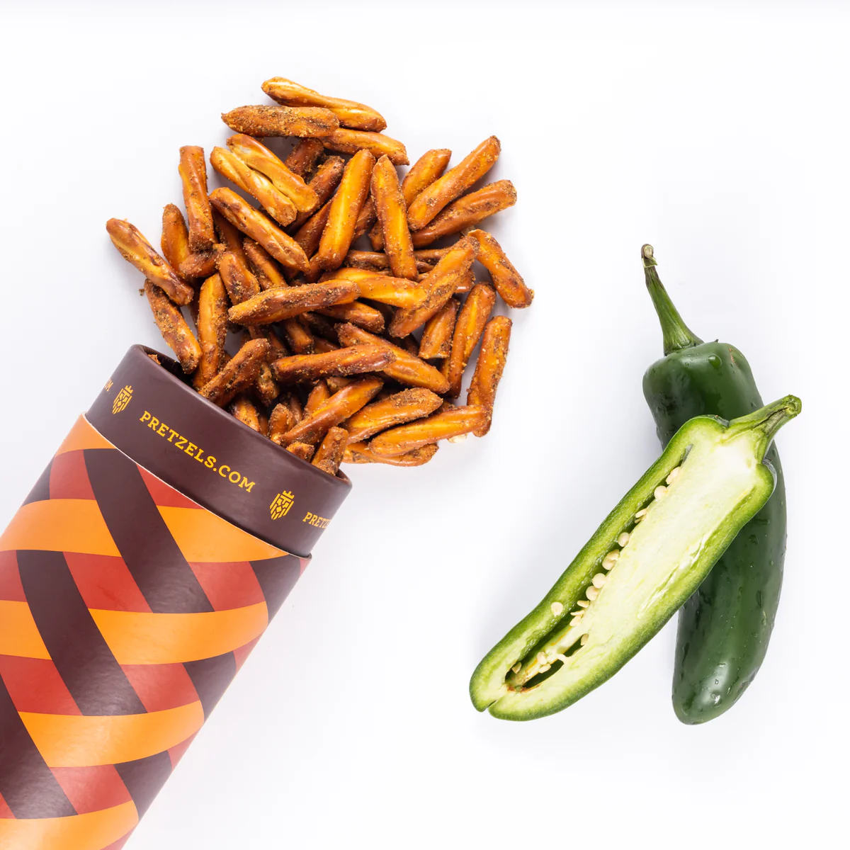 Pretzel sticks spill from a container next to a sliced jalapeño.