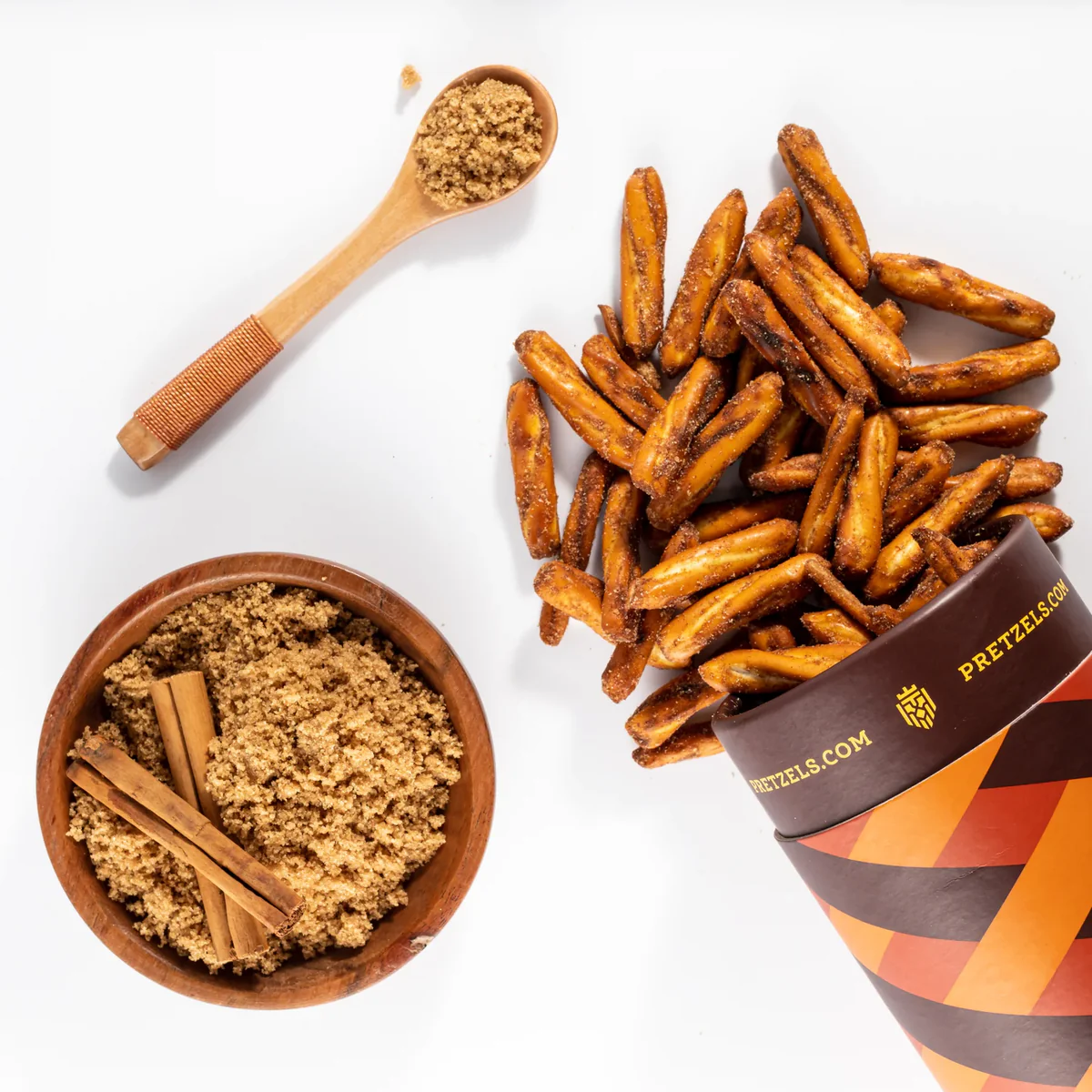 Cinnamon sticks and brown sugar beside a spilled container of pretzels.