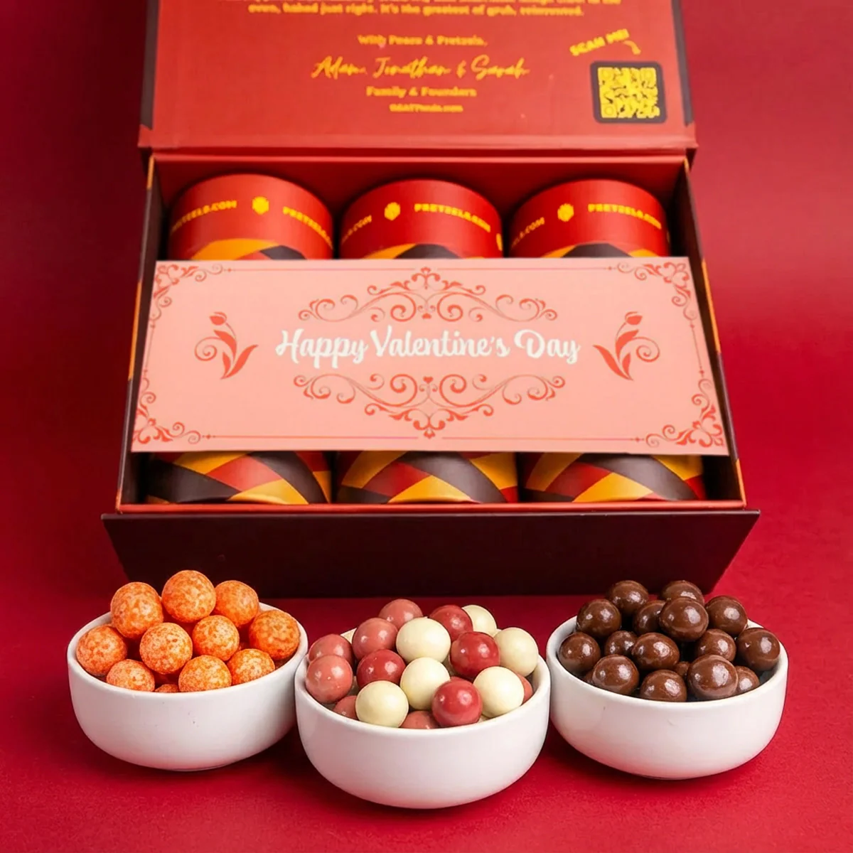 A Valentine's Day gift box with three small white bowls of colorful, round candies in front.