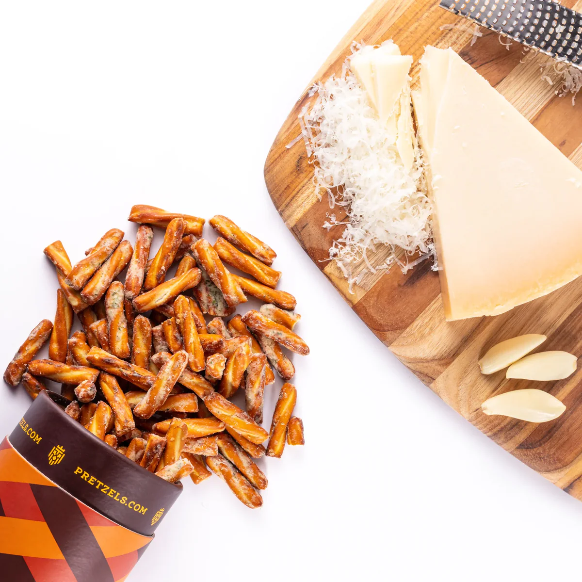 Pretzel sticks beside a cutting board with cheese wedges and grated cheese.