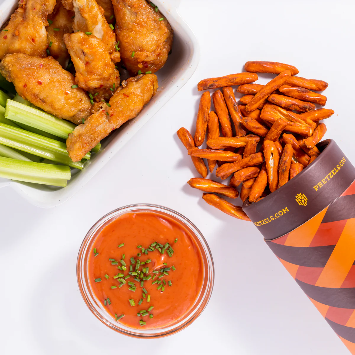 Chicken wings with celery, pretzel sticks, and red sauce in a glass bowl.