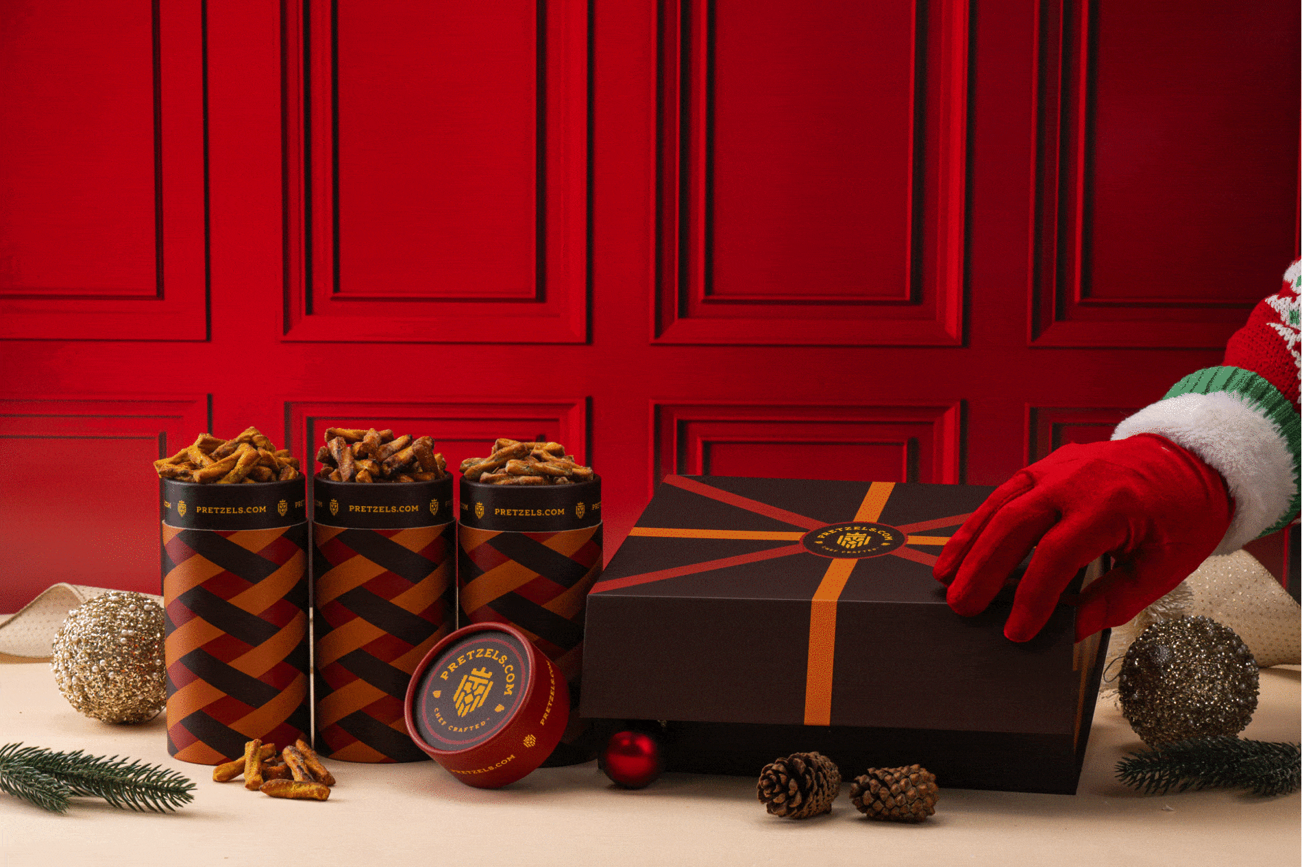 Gift box and pretzel containers with festive decorations and red background.