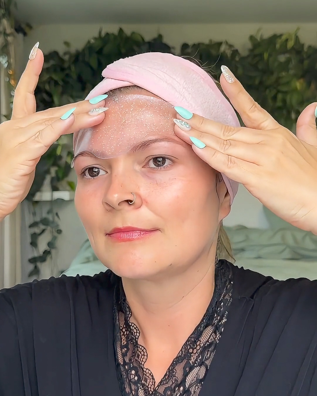 A woman with a pink headband applies a clear, shimmery gel product to her forehead.