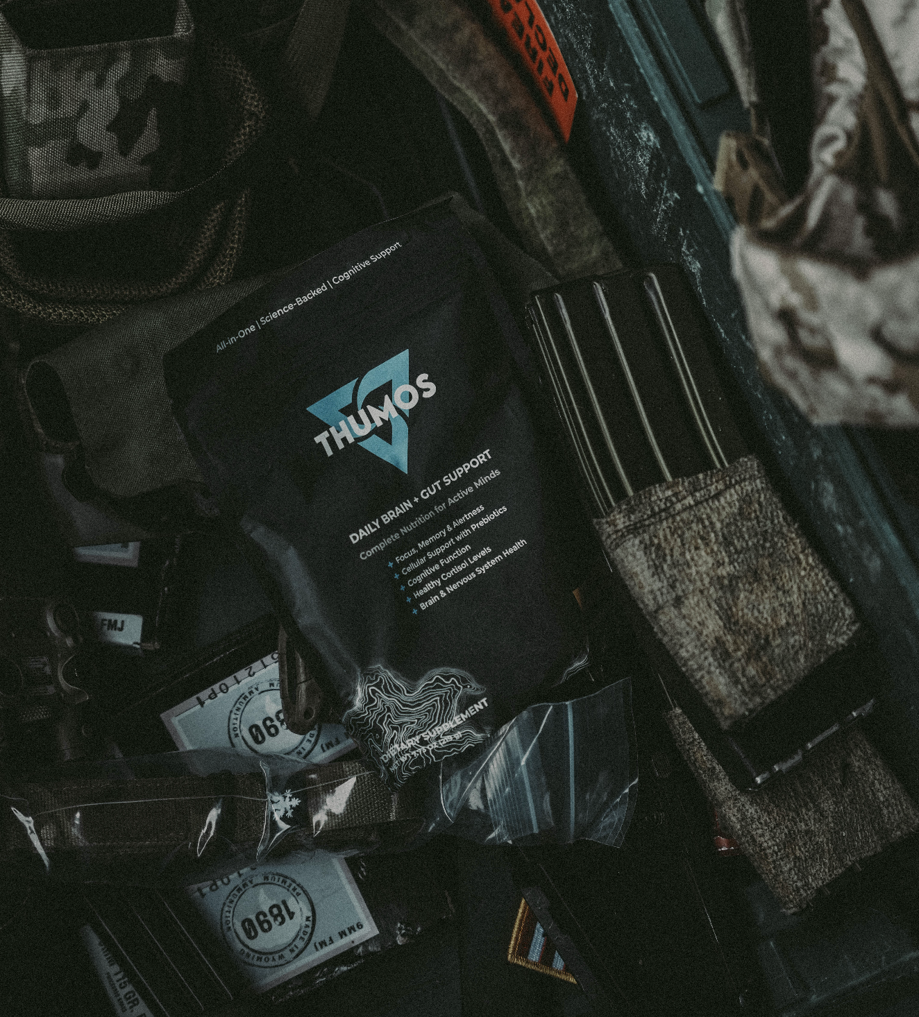 A dark, overhead shot of a pouch of THUMOS supplements sitting in a tactical case with ammunition.