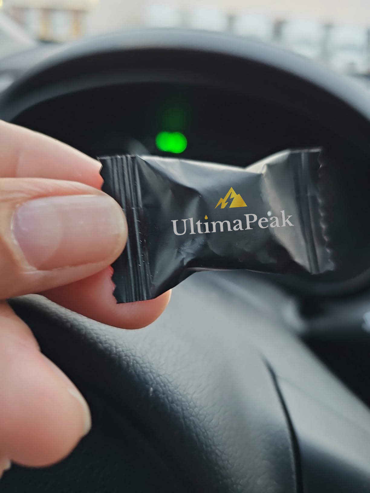 Hand holding a black candy wrapper labeled 'UltimaPeak' inside a car.