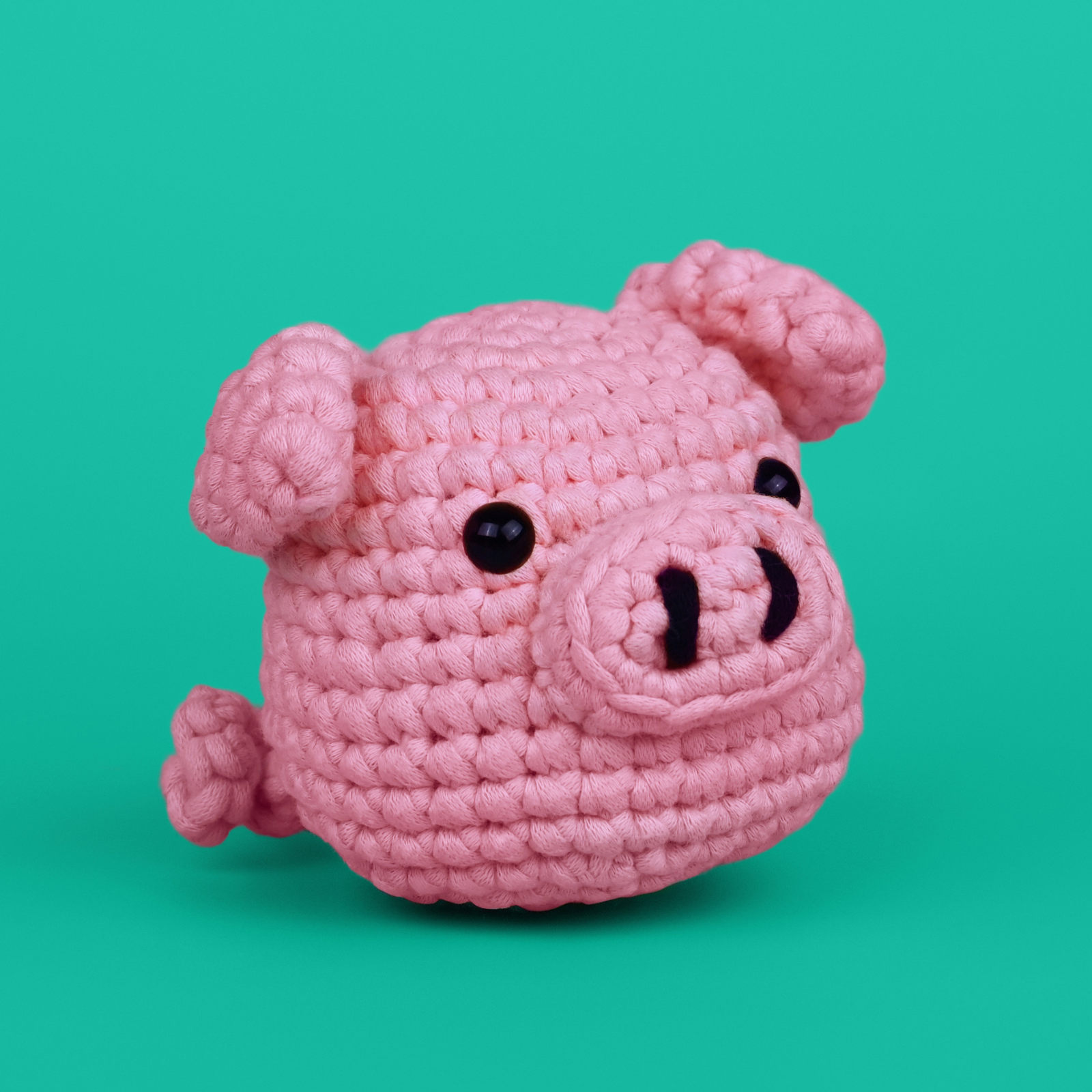 Pink crocheted pig toy on a teal background.