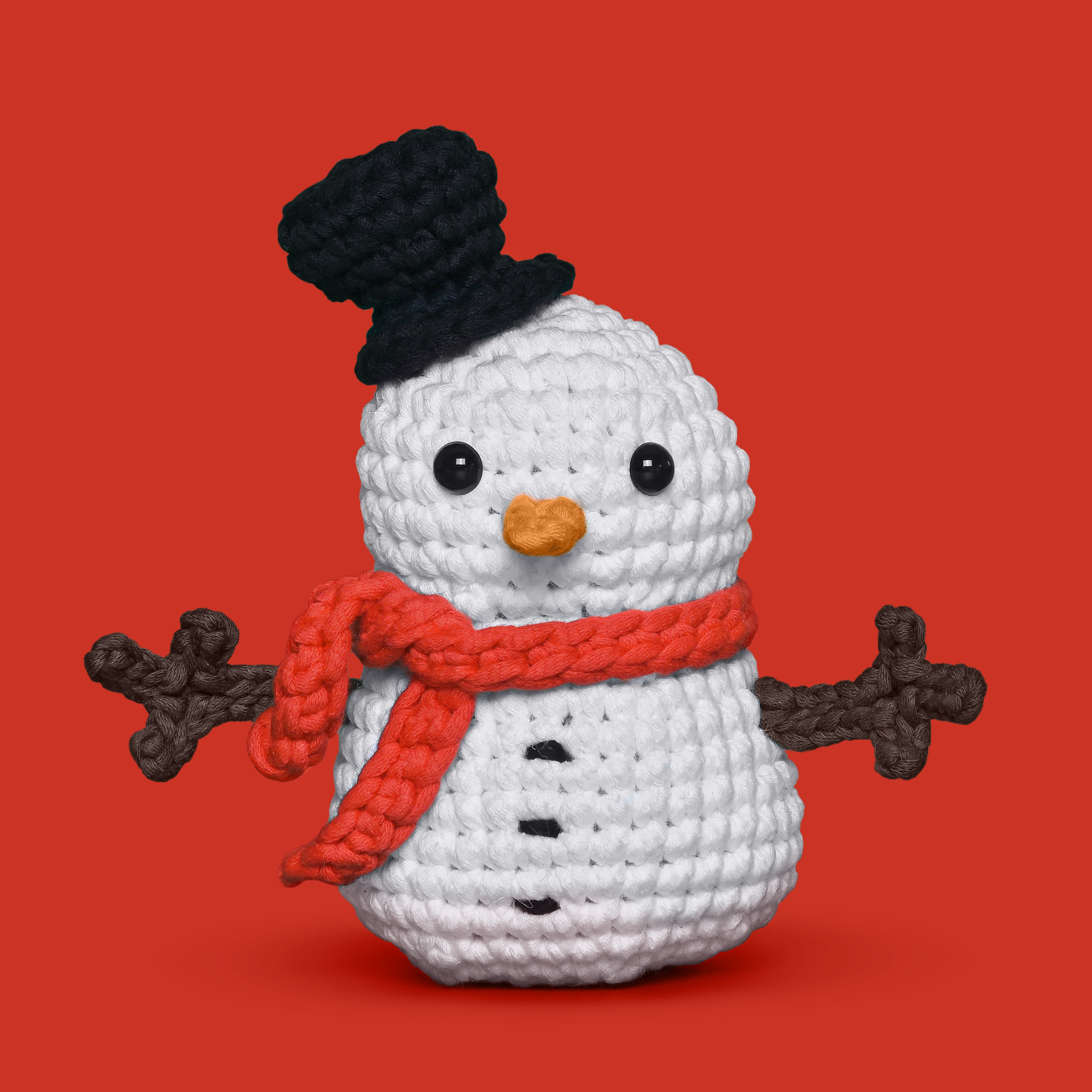 Crocheted snowman with black hat, orange scarf, on red background.