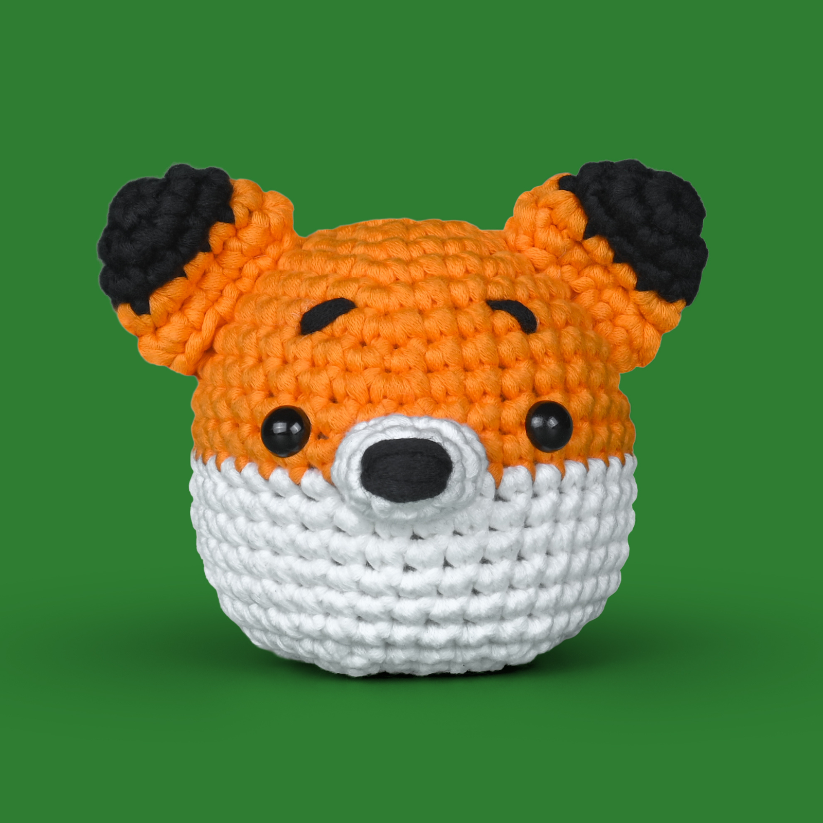 Crocheted kawaii-style orange and white fox with black eyes on a green background.