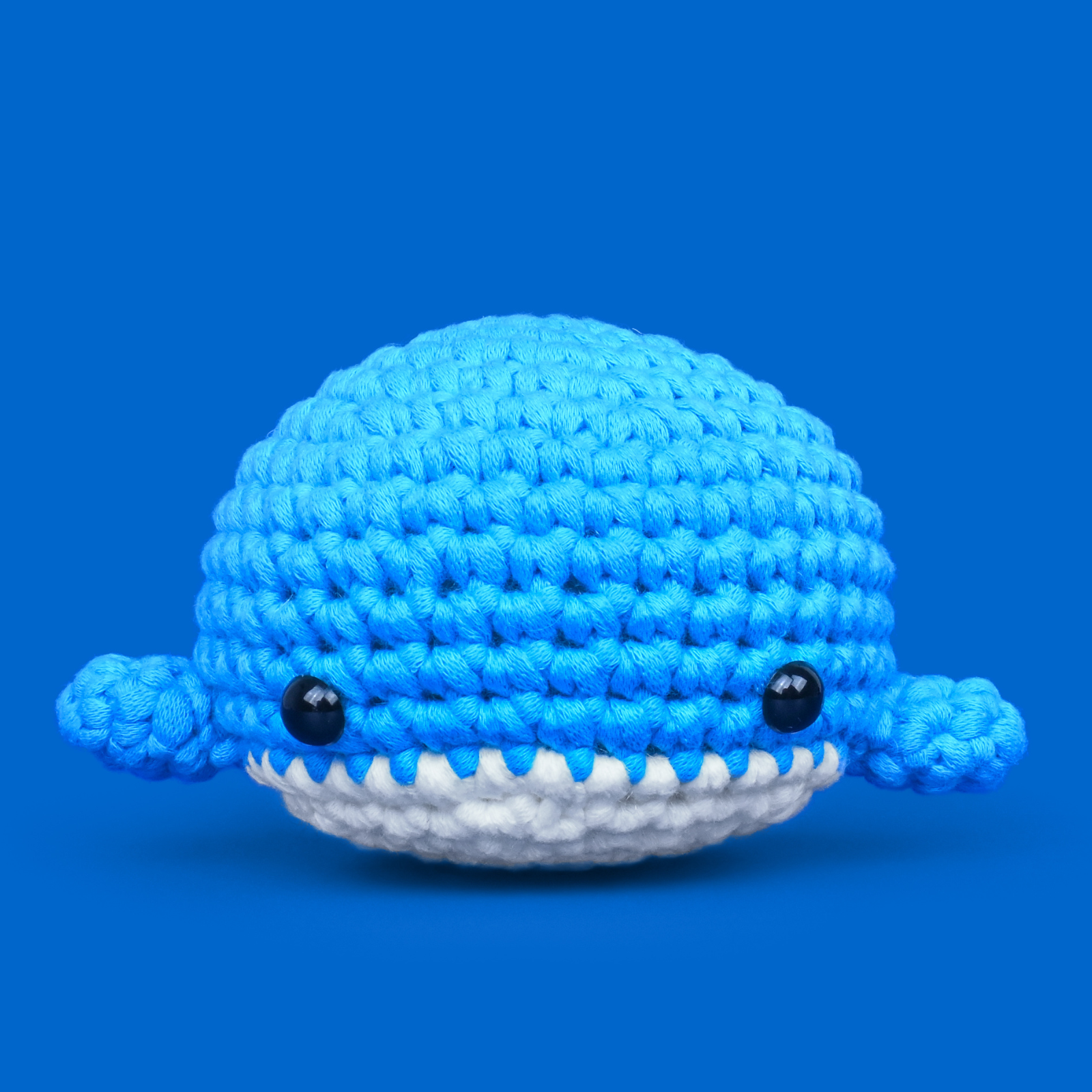 Blue crocheted whale toy with small black eyes.