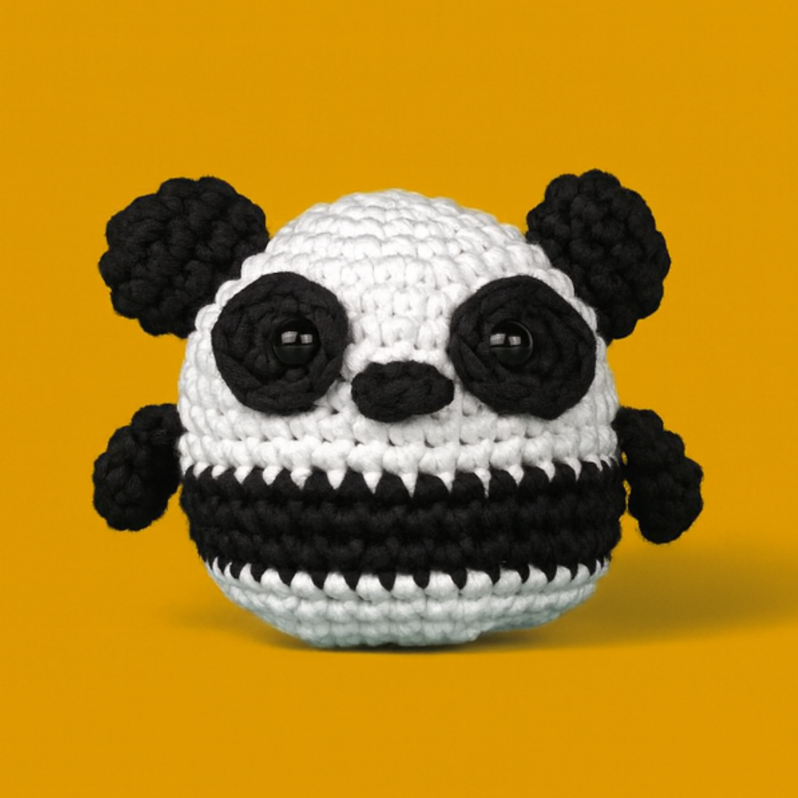 Crocheted panda toy with black and white yarn on an orange background.