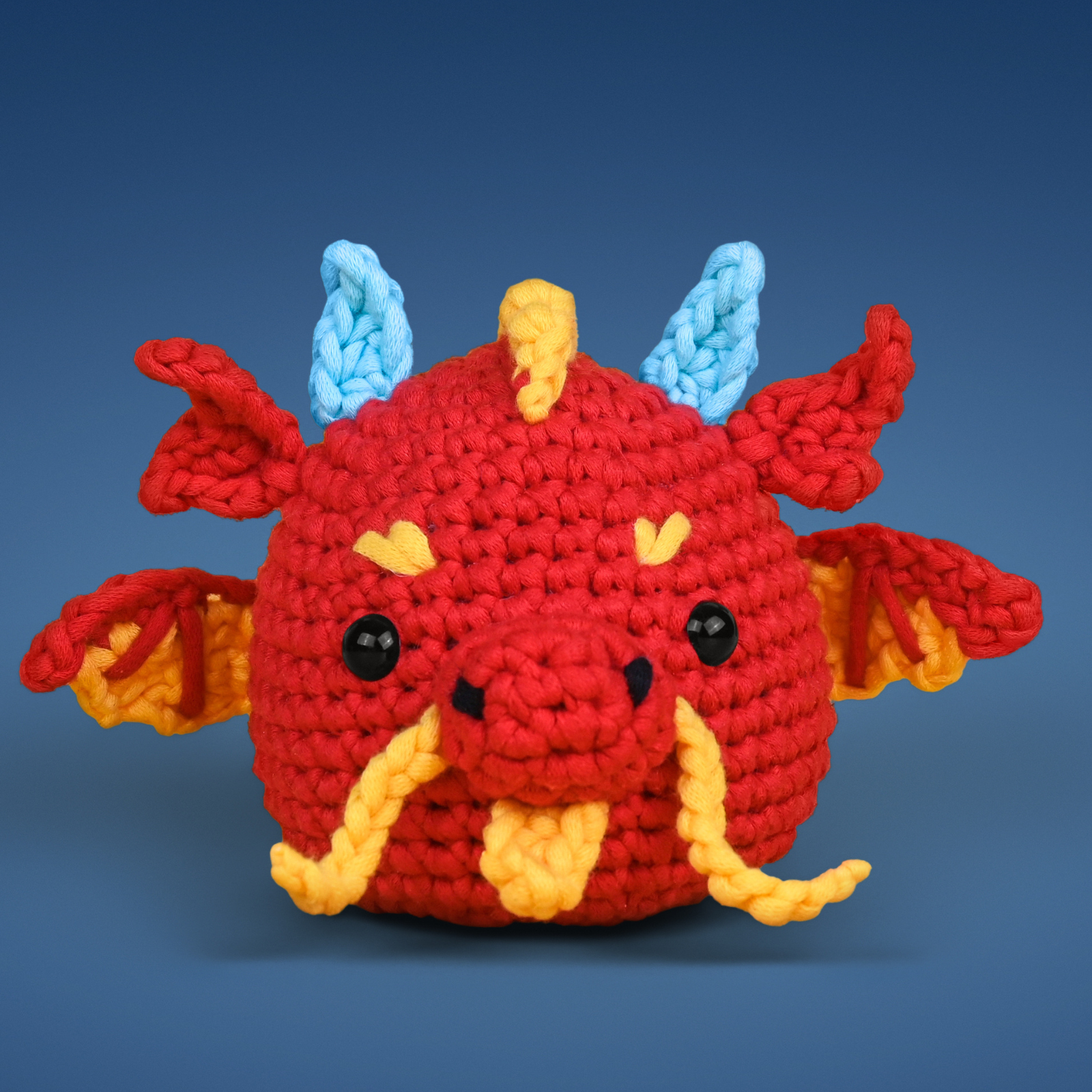 Crocheted red dragon toy with blue horns and yellow accents on a blue background.