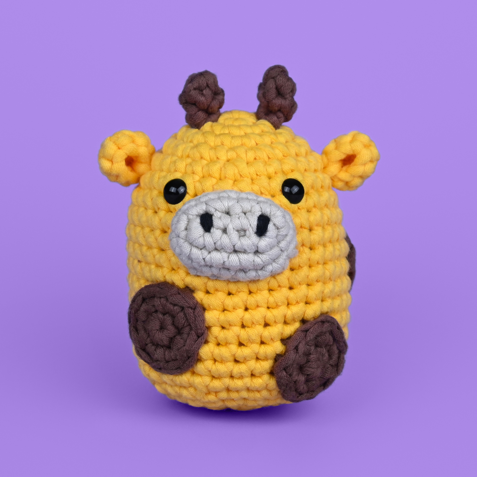 Crocheted giraffe toy with black eyes on a purple background.