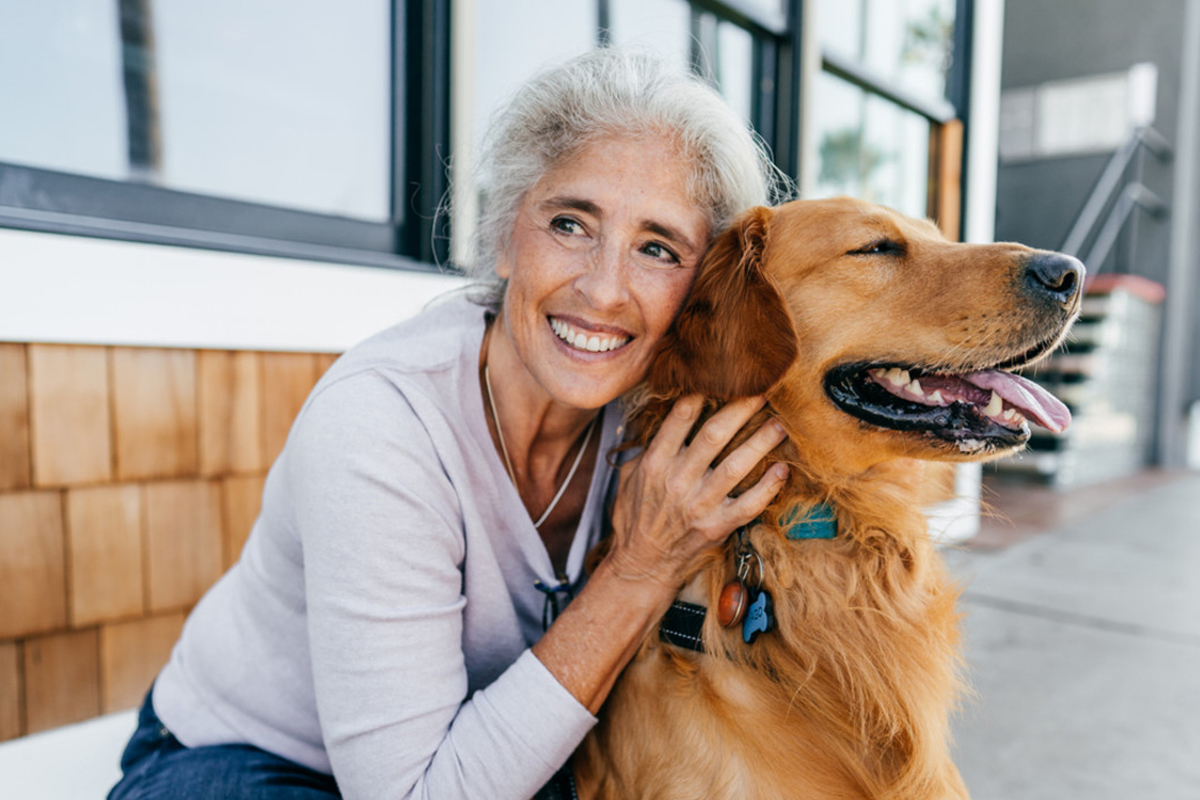 Smiling person with a Golden Retriever dog outside a building.