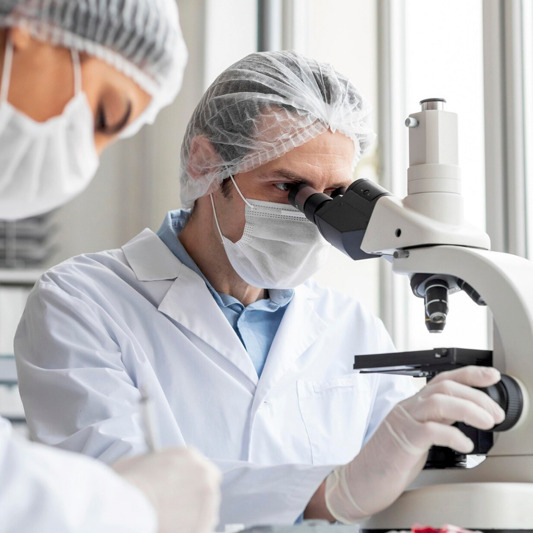 Scientists in lab coats and masks using a microscope.
