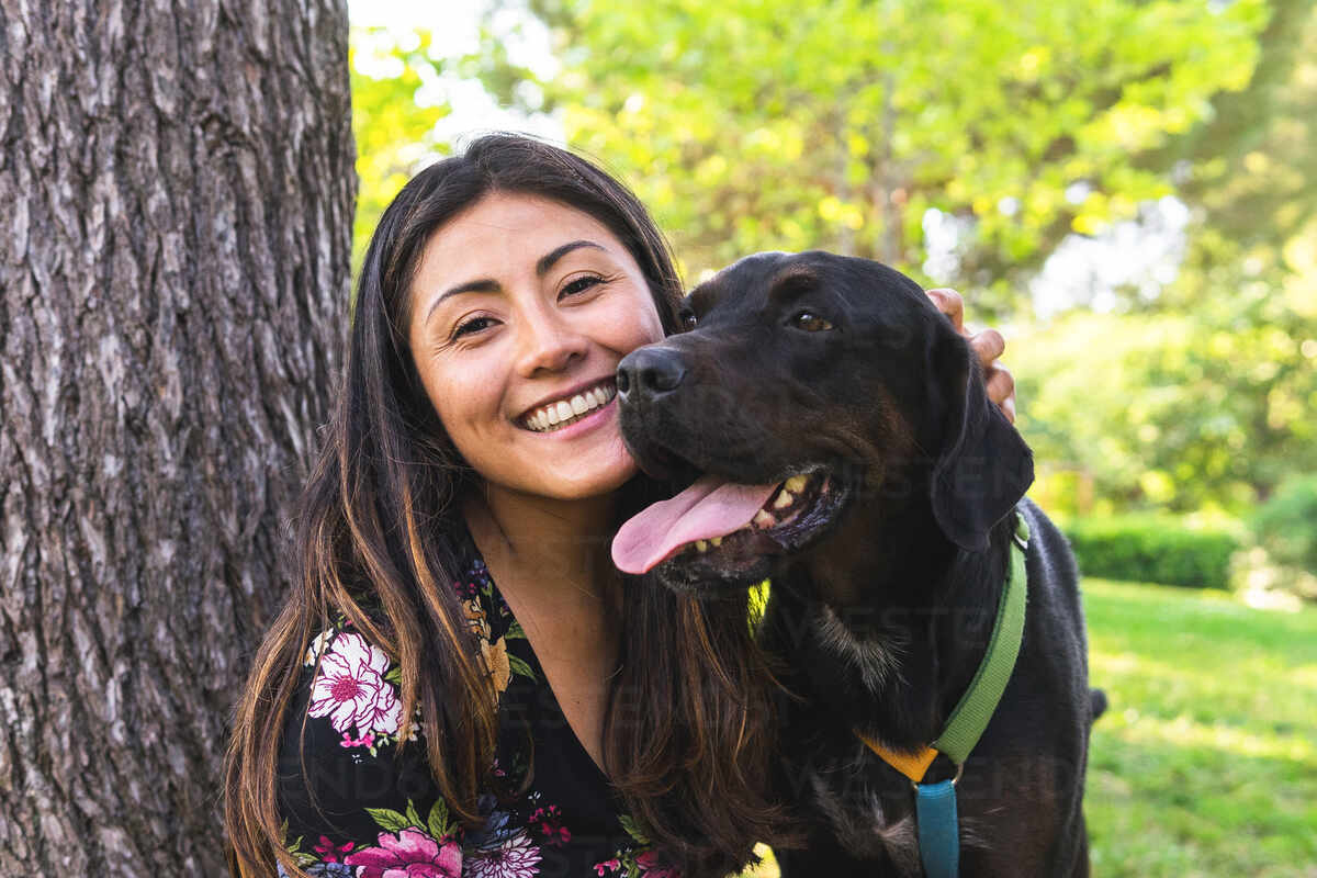 Smiling woman with a dog in a park setting.