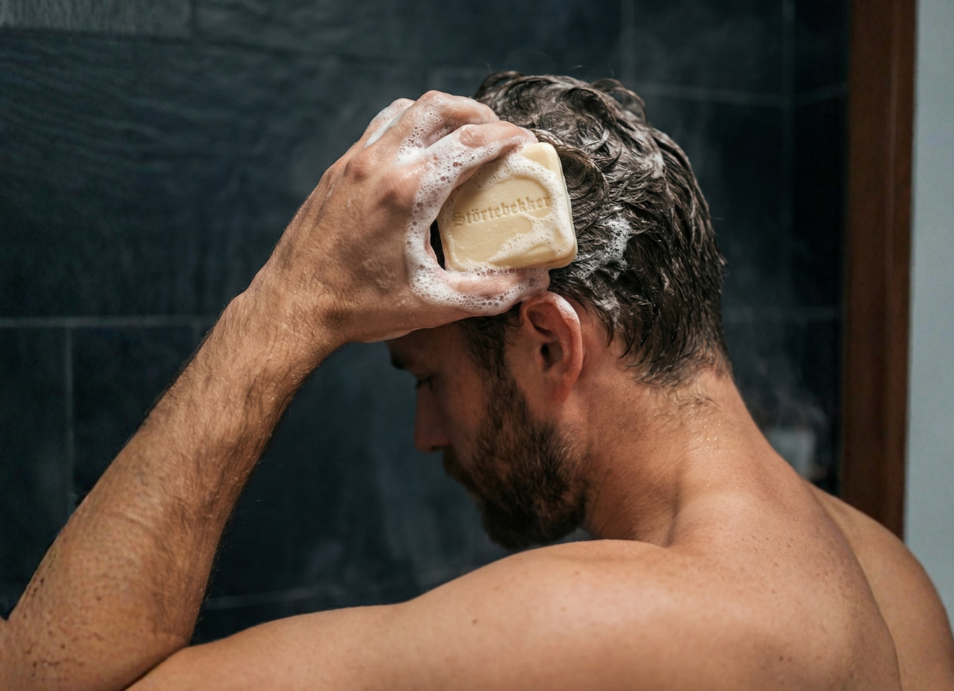 A man seen from behind washes his hair with a sudsy bar of soap.