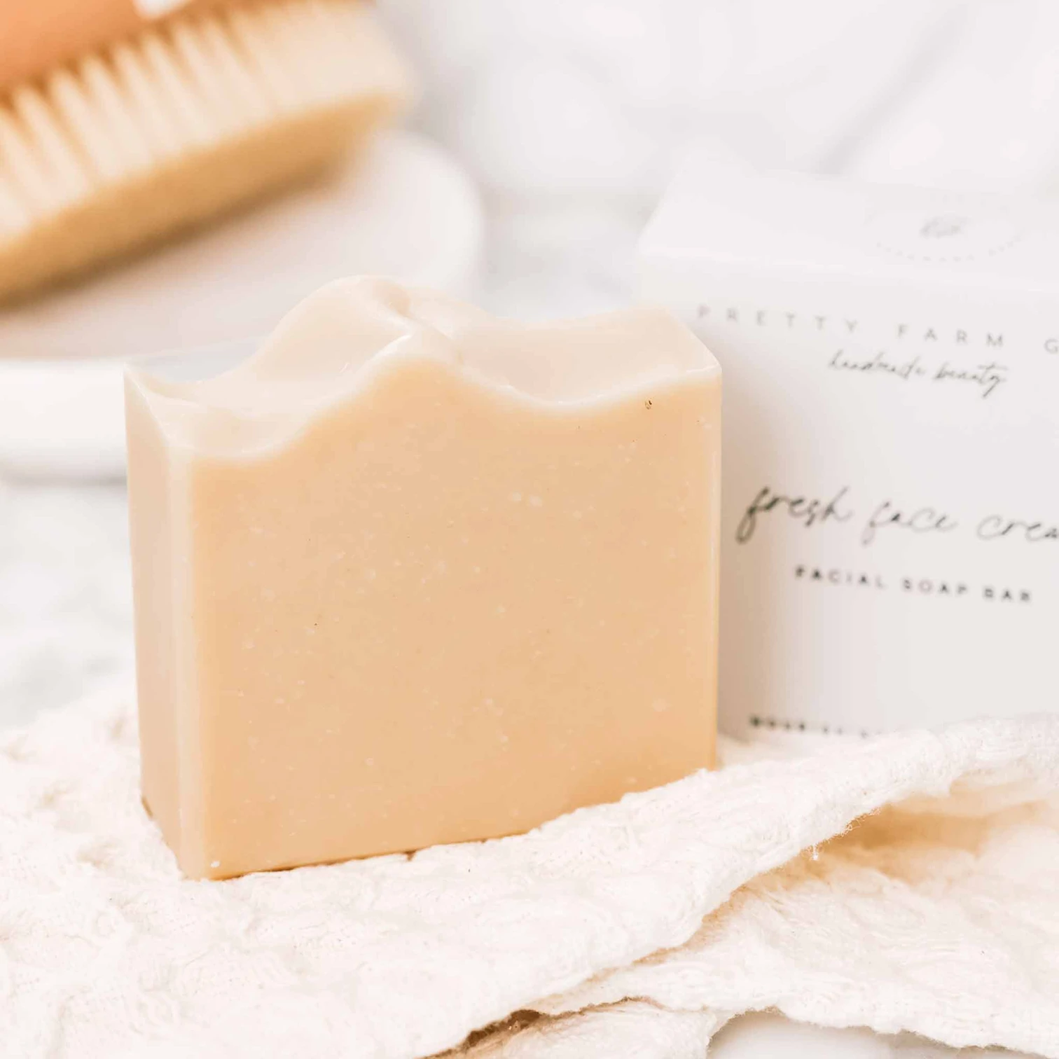 A handmade bar of facial soap on a cloth in front of its box and a wooden brush.