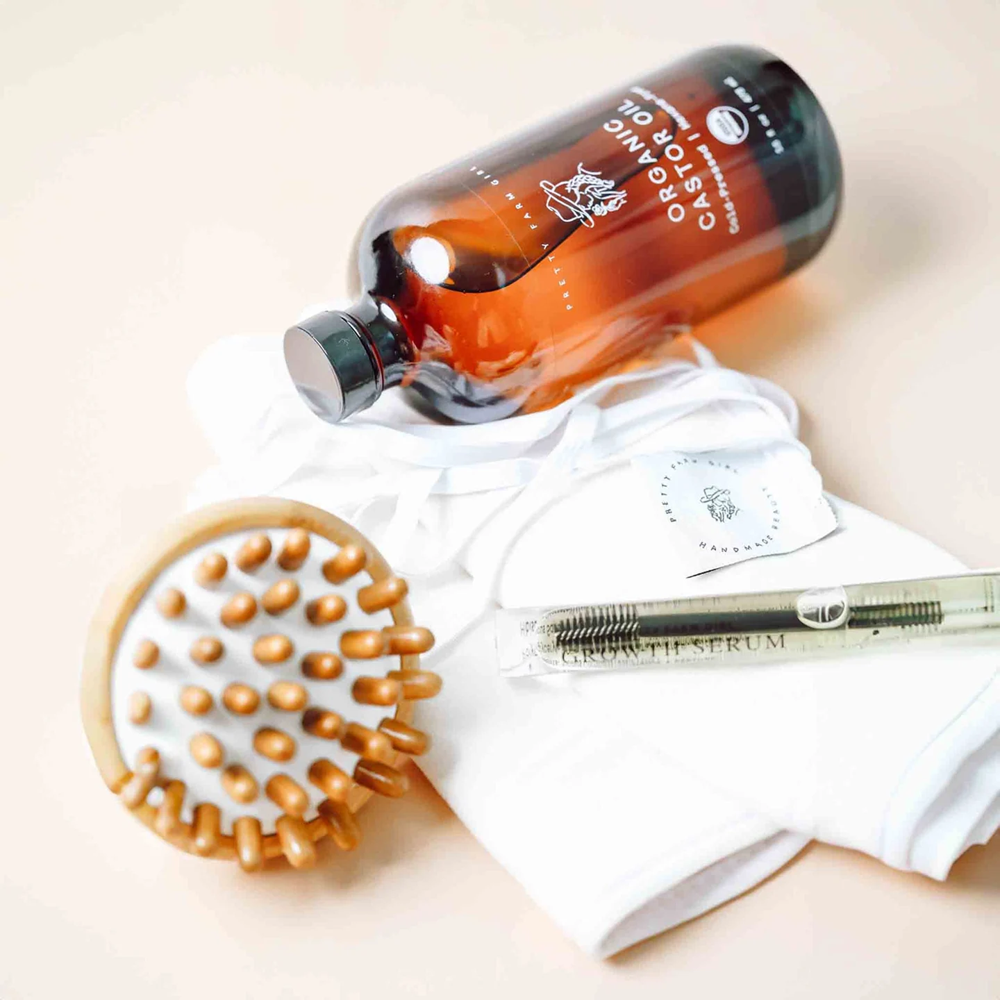 A bottle of organic castor oil, a growth serum, and a scalp massager on a white cloth.