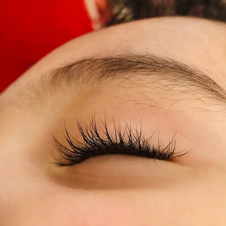 A close-up of a closed eye with long, dark eyelash extensions and a well-defined eyebrow.