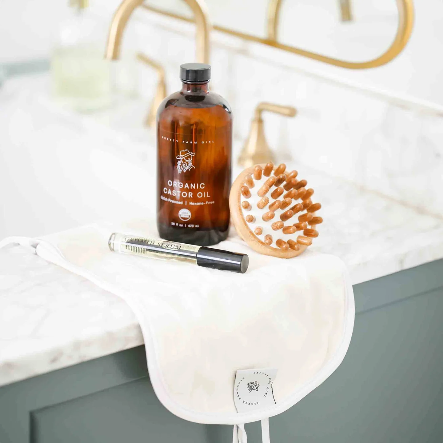A bottle of organic castor oil, a growth serum, and a scalp massager on a bathroom counter.