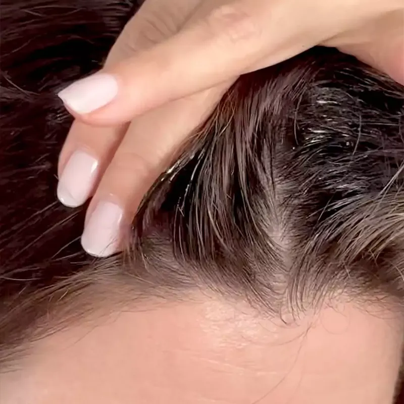 A close-up of a hand with a light-colored manicure running through dark, wet hair at the scalp.