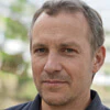 Portrait of a middle-aged man with short hair, wearing a dark shirt, outdoors.