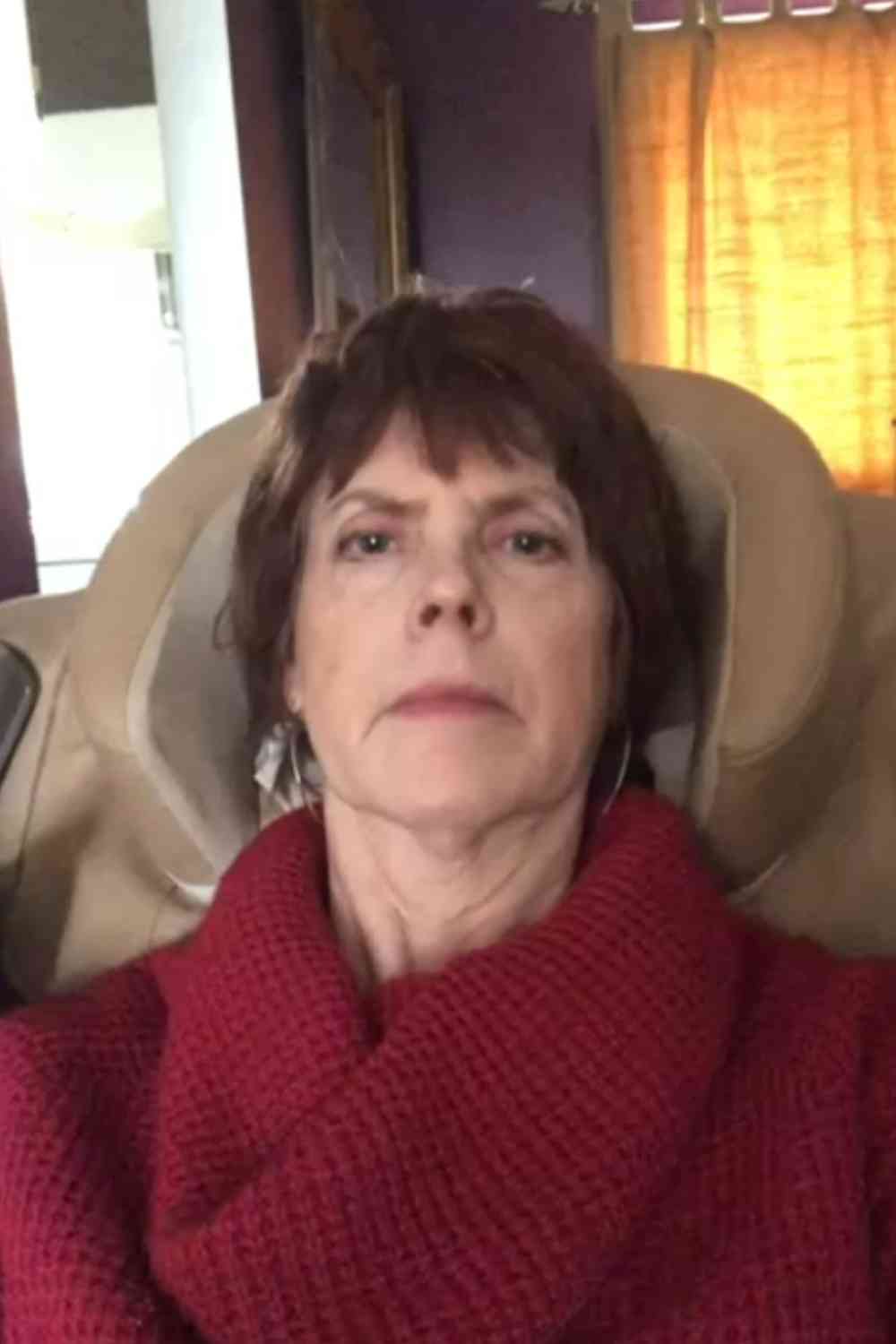 Person in a red sweater sitting indoors with a neutral expression.