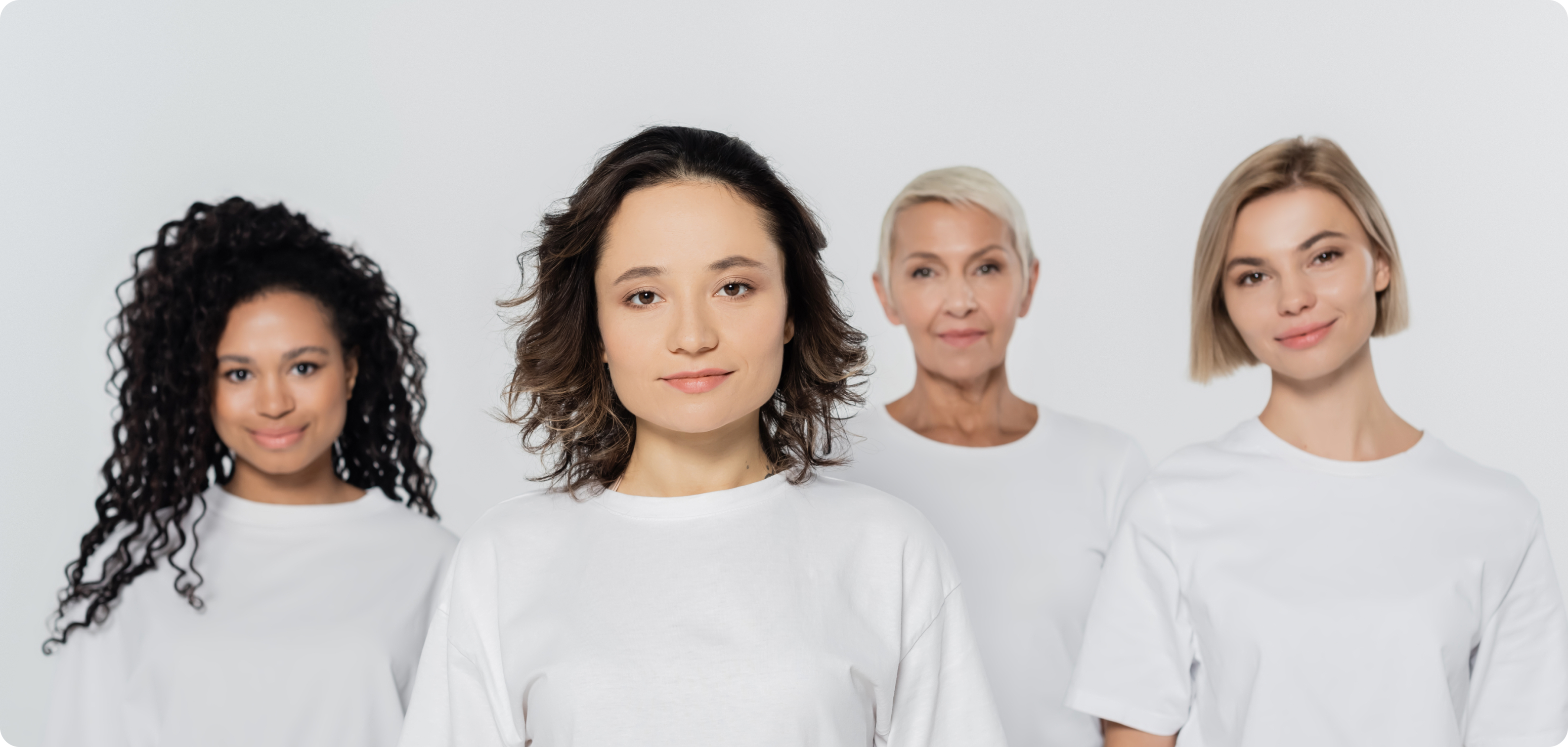 Four women in white shirts standing together against a white background.