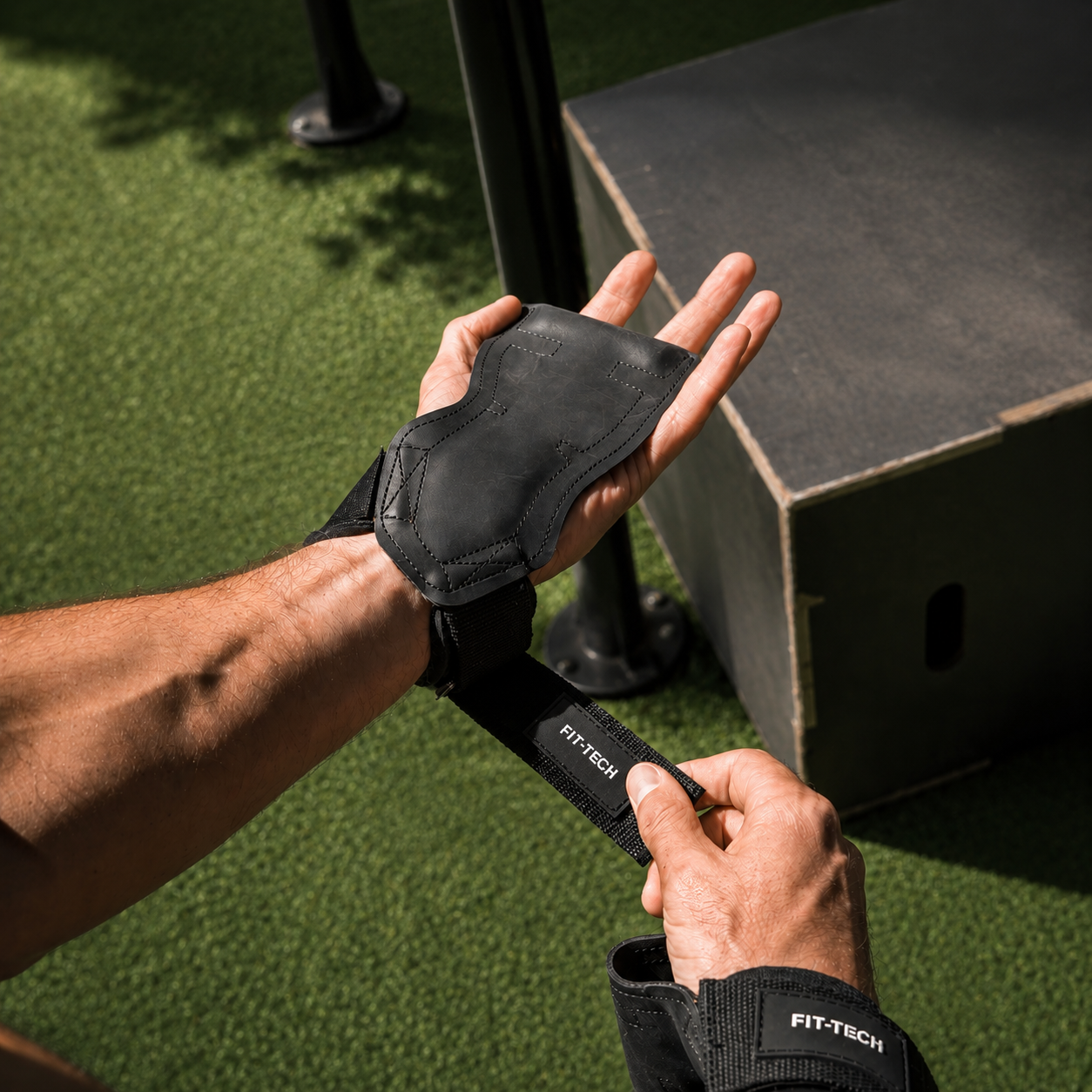 A close-up of a person putting on black Fit-Tech workout hand grips with wrist wraps.