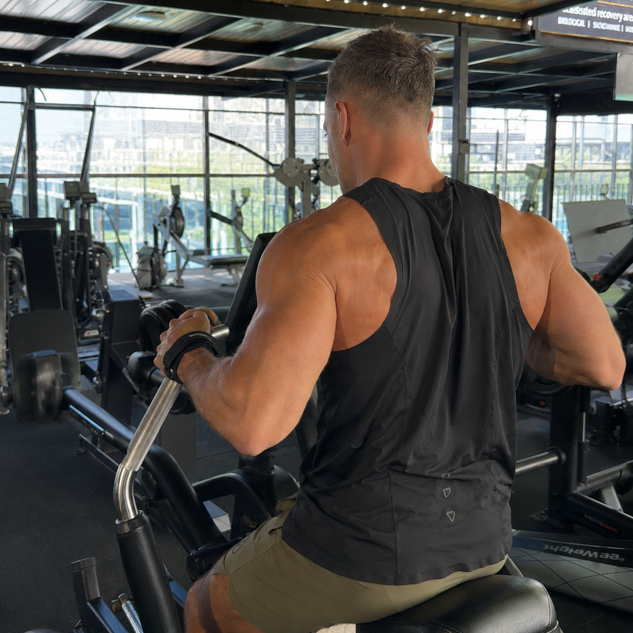 A muscular man, seen from behind, using a seated row machine at the gym.