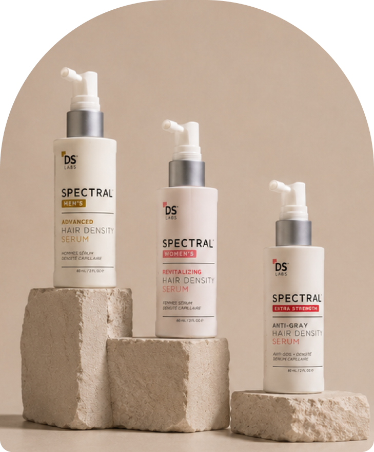 Three bottles of DS Labs Spectral hair density serum arranged on stone blocks against a beige background.
