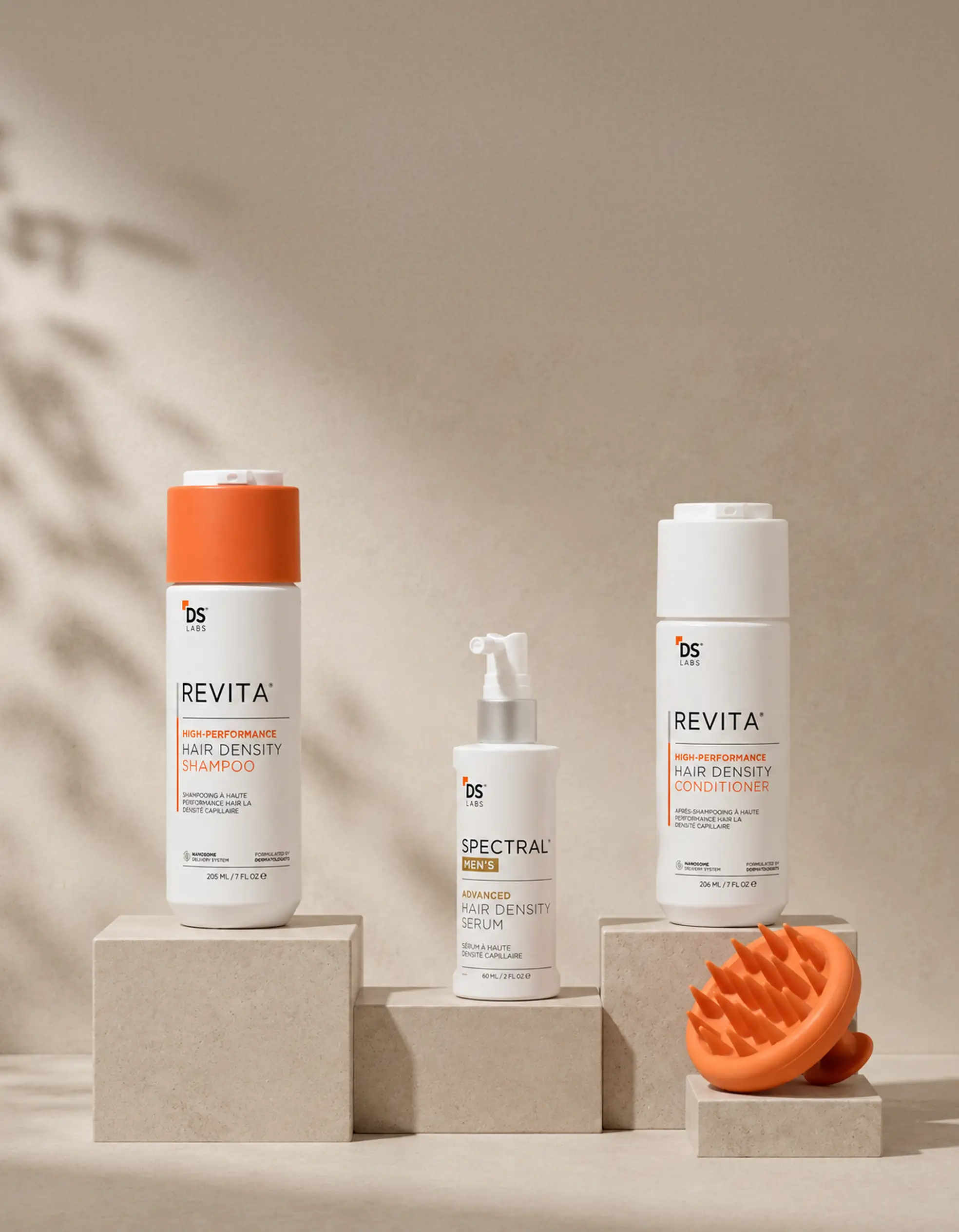 DS Labs hair density shampoo, conditioner, serum, and an orange scalp massager displayed on beige blocks.