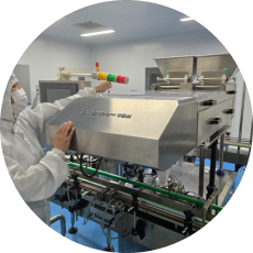 A person in a white cleanroom suit adjusts a signal light on a stainless steel production line machine.