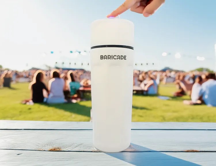 White bottle labeled 'BARICADE' with a finger pressing the top, outdoors with people in the background.