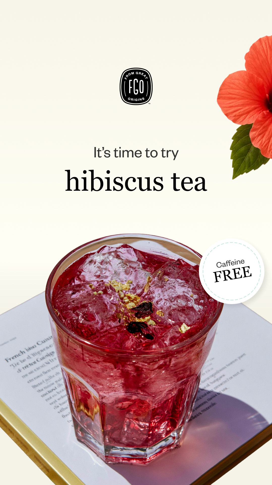 A glass of iced hibiscus tea sits on an open book next to a red hibiscus flower.