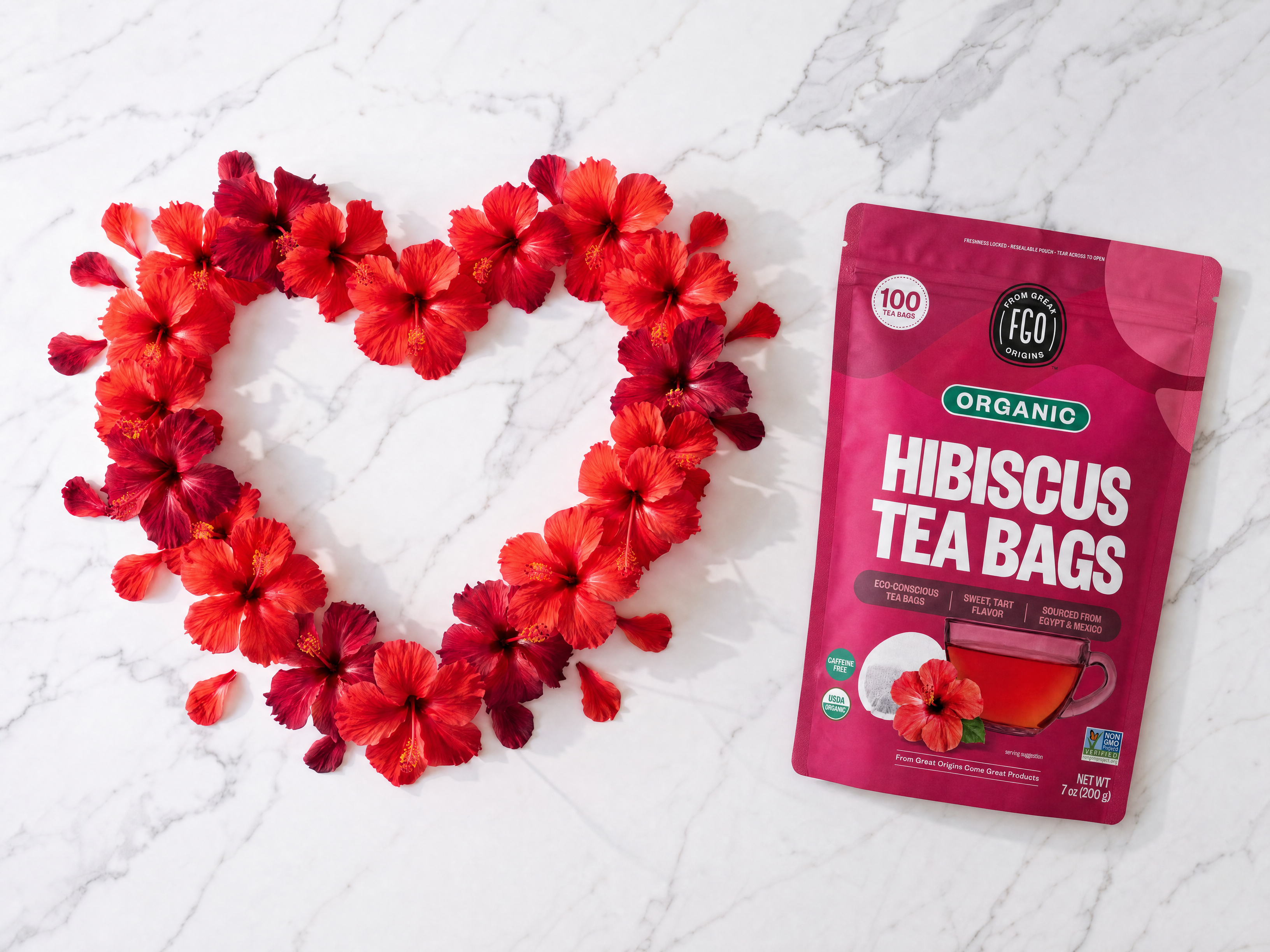 A pouch of hibiscus tea bags on a marble surface next to red hibiscus flowers in a heart shape.