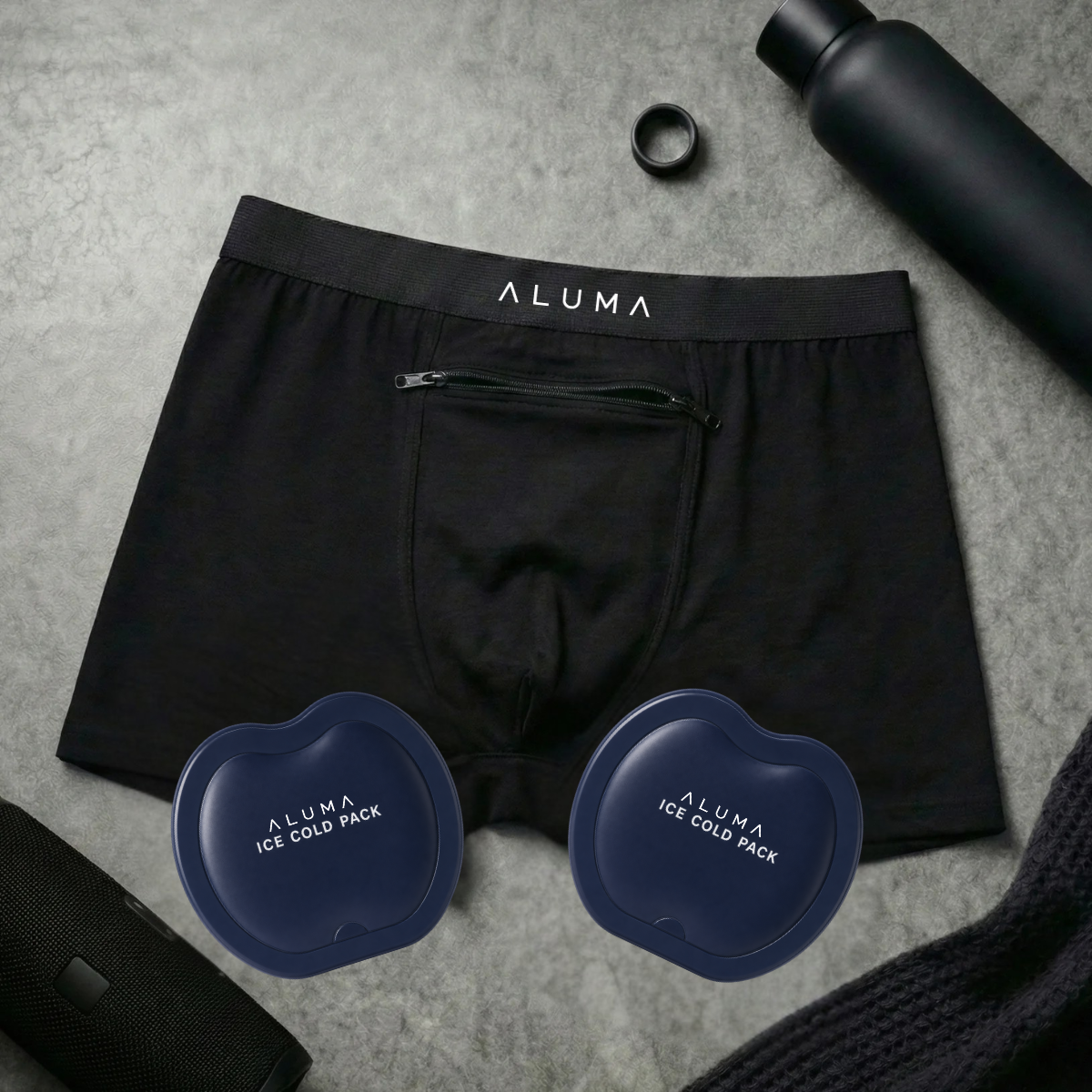 A flat lay of black Aluma boxer briefs, two ice cold packs, a water bottle, and other accessories.
