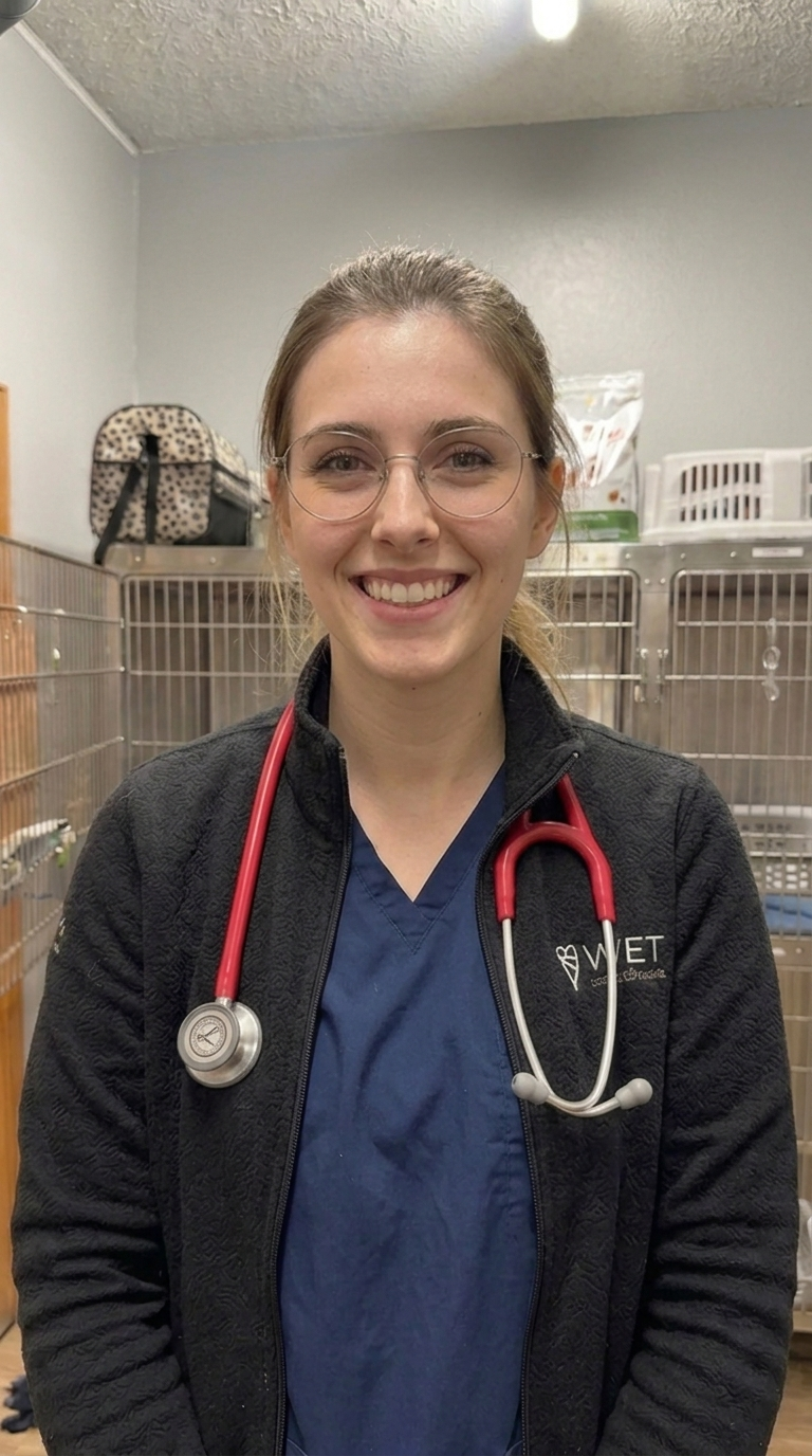 A smiling woman in scrubs and a fleece jacket with a red stethoscope around her neck.