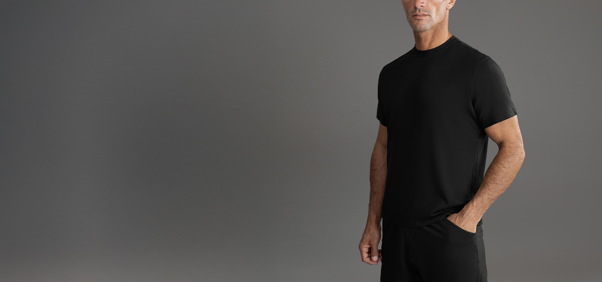 Man in a black t-shirt and pants against a gray background.