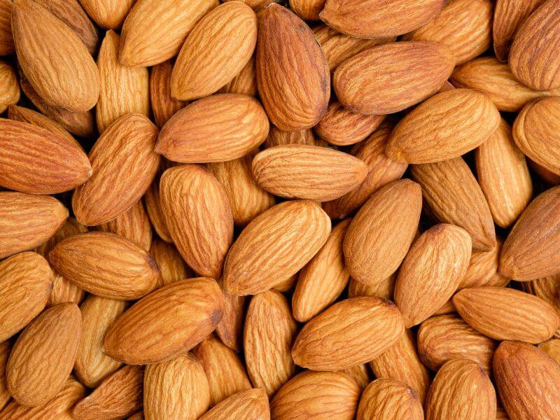 A close-up, top-down photograph of a pile of shelled, whole almonds.