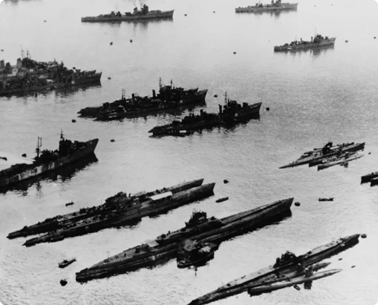 A black and white aerial photograph of numerous naval ships and submarines gathered in a harbor.