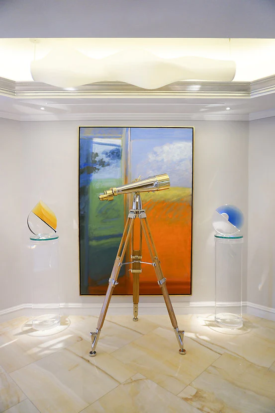 A telescope on a tripod in front of colorful abstract art, flanked by sculptures on pedestals.
