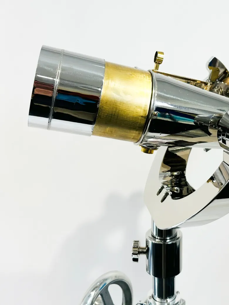 A close-up of a shiny chrome and brass telescope mounted on an adjustable stand against a white background.
