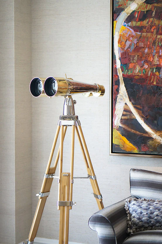 Vintage binoculars on a wooden tripod next to an abstract painting.