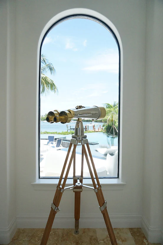 Brass telescope on a wooden tripod stand in a room.