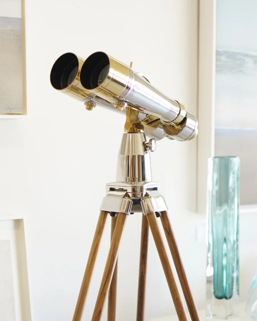 Brass telescope on a wooden tripod stand in a room.