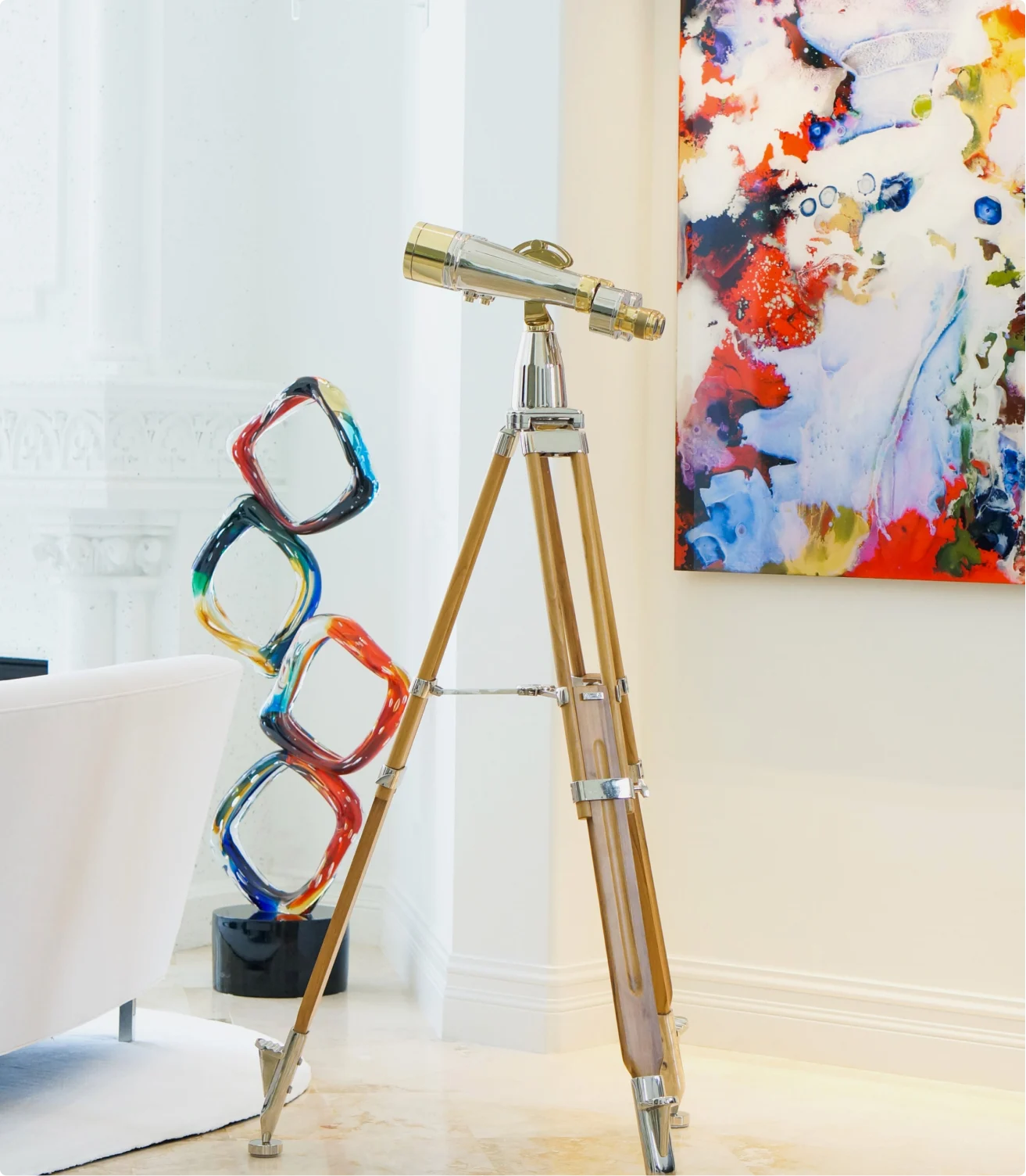 A vintage-style telescope on a tripod stands in a brightly lit room next to modern art.