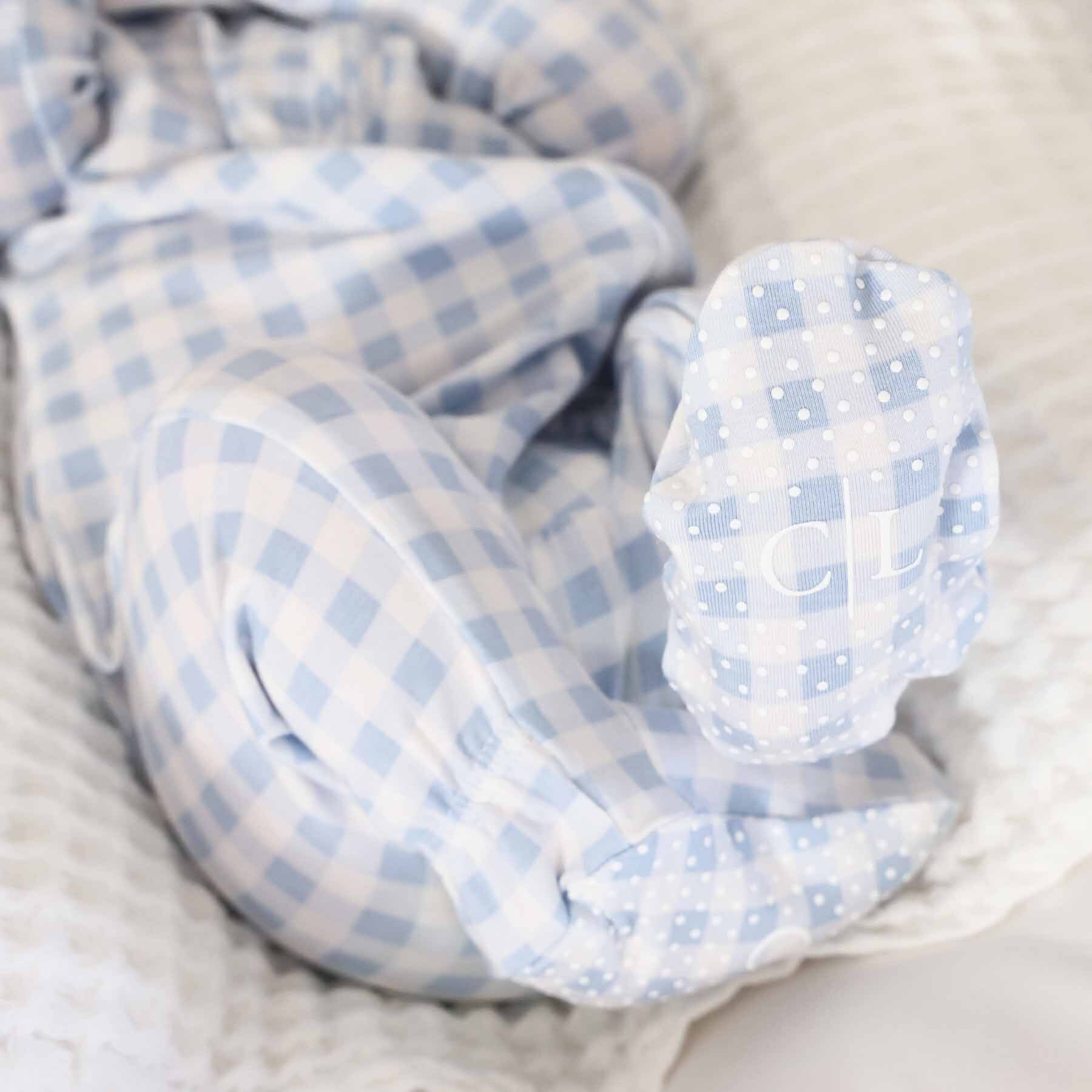 Baby wearing blue and white checkered pajamas with initials on the foot.